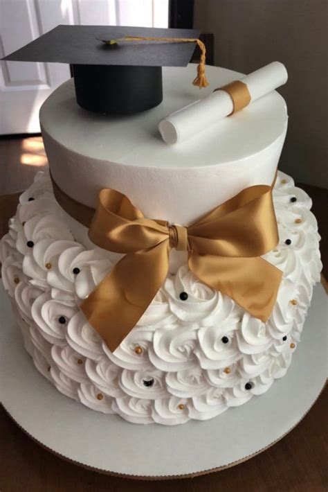 A Graduation Cake Is Decorated With White Frosting And Gold Ribbon Topped With A Mortar And Tassel