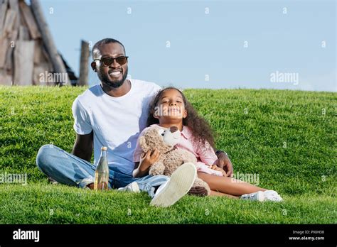 Happy African American Father And Daughter Sitting On Hill With Soda