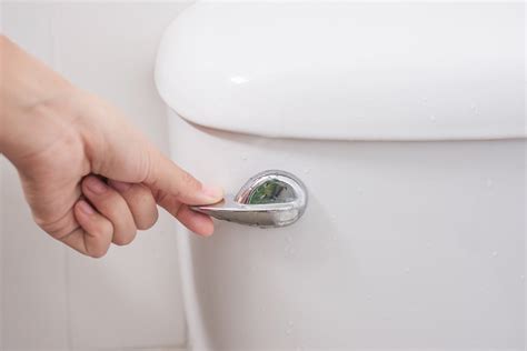 A Hand Flushing A White Porcelain Toilet