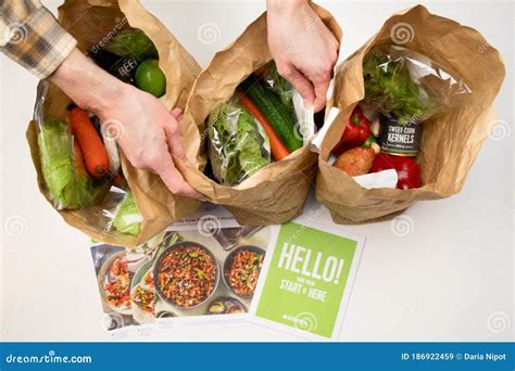 Hands Opening Hello Fresh Meal Kits In A Paper Bags On A White Table