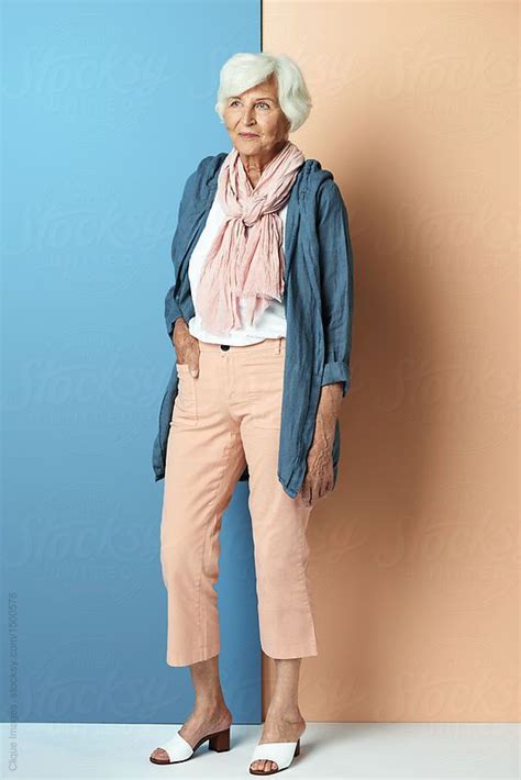 An Older Woman Standing In Front Of A Blue And Pink Wall With Her Hands On Her Hips