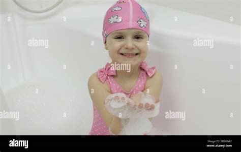 Attractive Four Years Old Girl Takes A Bath With Bath Foam In Pink Swimwear And Swimming Cap