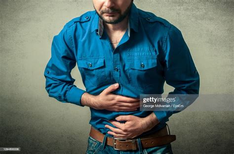 Midsection Of Mid Adult Man Suffering From Stomachache Against Gray