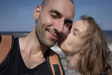 Loving Girlfriend Kissing Smiling Boyfriend On Cheek At Beach During