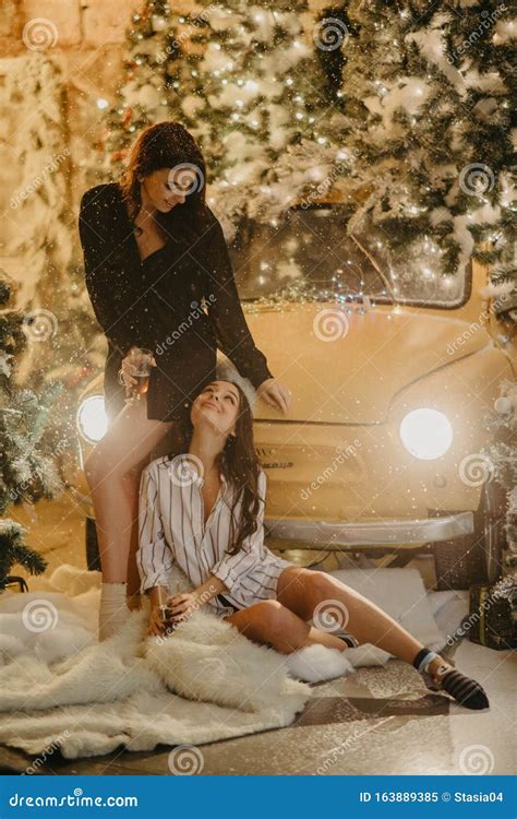 Lesbian Couple Holds Glasses Of Wine Against Background Of Christmas Decorations Snowfall And