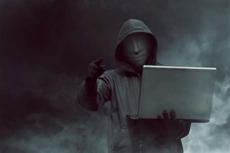 Premium Photo Portrait Of Hooded Hacker With Mask Holding Laptop
