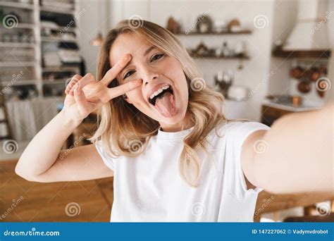 image closeup of attractive blond woman showing peace sign while taking selfie photo at home