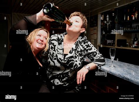 Two Drunken Middle Aged Woman Drinking Champagne From The Bottle In A