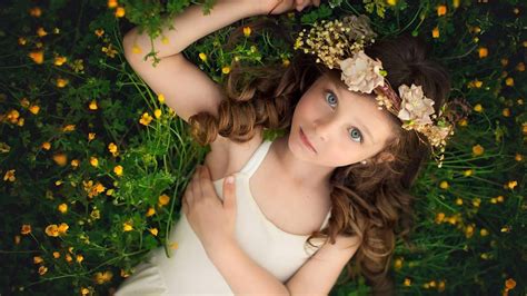 Cute Little Girl Is Lying On Yellow Flower Plant Looking Up Wearing