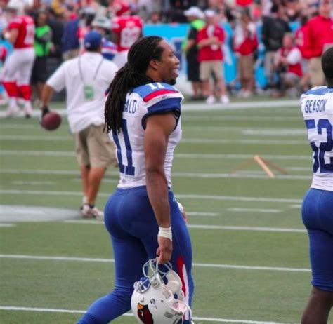 two football players are standing on the field with helmets in their hands and people behind