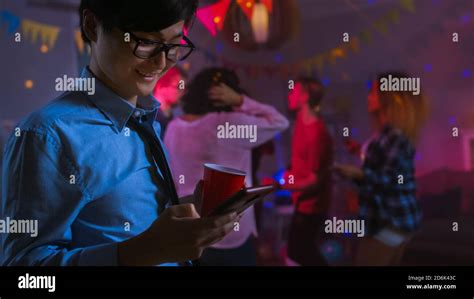 at the wild house party happy asian man uses smartphone instead of dancing with other people
