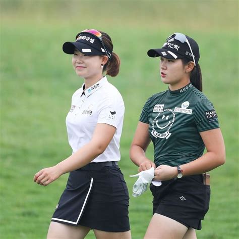 Two Female Golf Players Walking In The Grass With Their Hats On And One