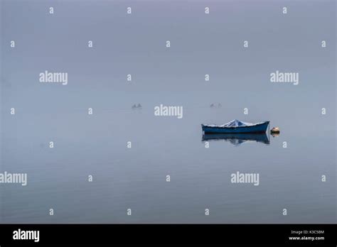 Boat On Calm Lake Water In A Foggy Morning With Other Fishing Boats In