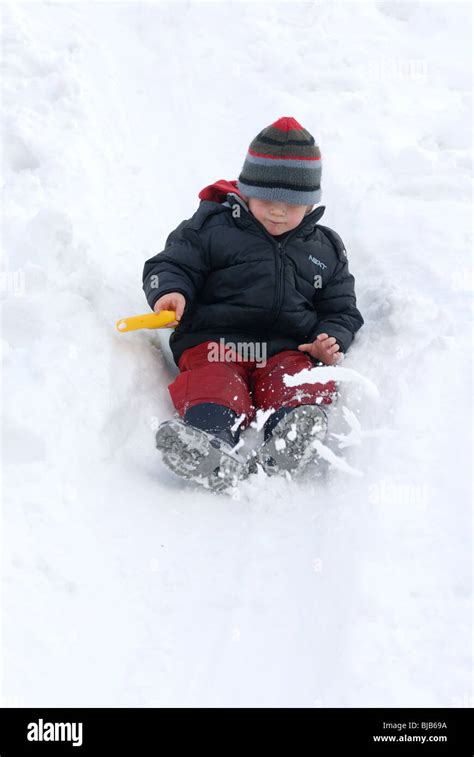 Laughing Child Boy Sliding Down A Snow Covered Hill And Playing In Snow