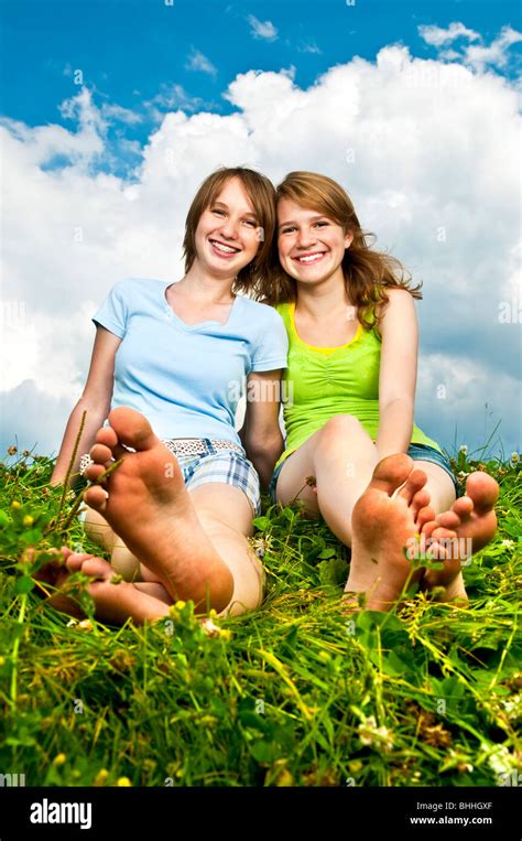 Two Young Teenage Girl Friends Sitting Barefoot On Summer Meadow Stock