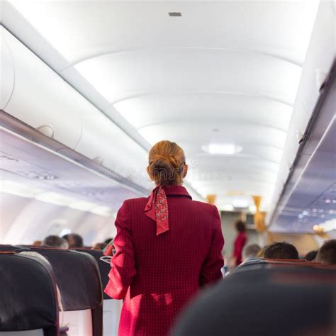 Stewardess In Red Uniform Walking The Aisle Of Commercial Airplane