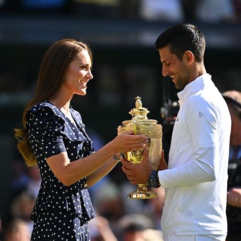 A Man Holding A Trophy Next To A Woman In Front Of A Crowd On A Tennis