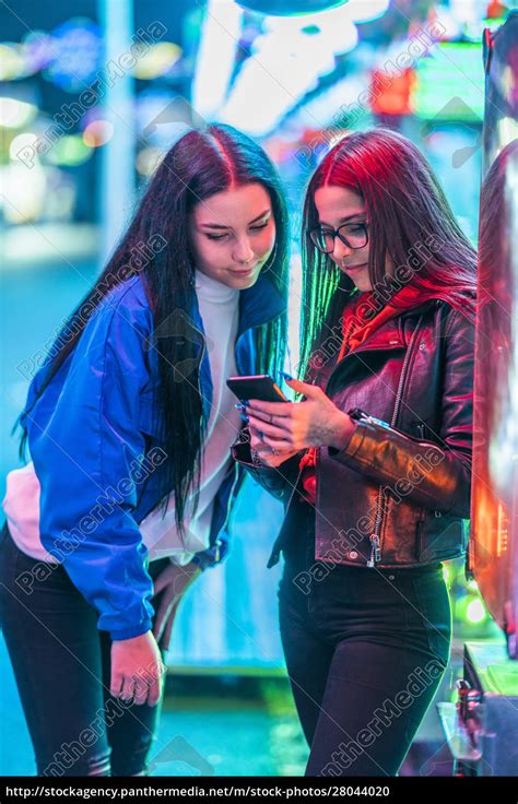 Two Teenage Girls Sharing Smartphone On A Funfair At Royalty Free Photo 28044020