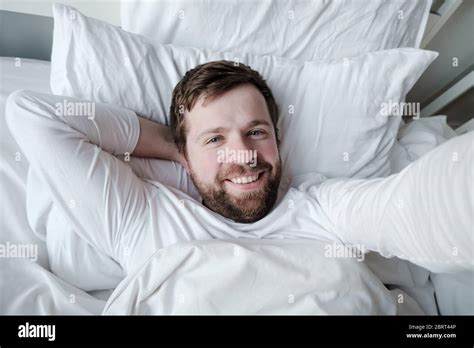 Happy Smiling Man Takes A Selfie While Lying In Bed On A Soft Pillow In The Morning In