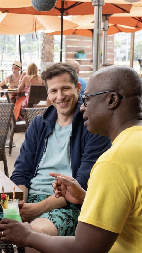 Two Men Sitting At An Outdoor Table Talking To Each Other And One Is Holding A Small Cake