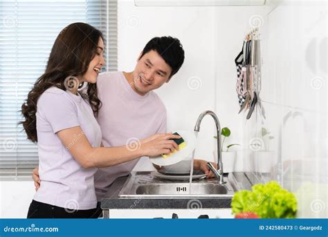 Happy Couple Washing Dishes Together In The Sink In The Kitchen At Home