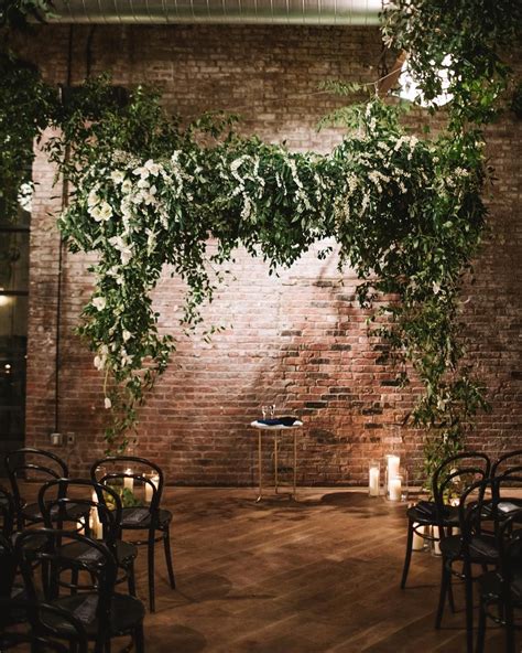 Greenery Ceremony Arch With A Rustic Brick Wall Backdrop