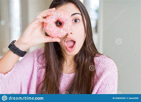 Beautiful Young Woman Eating Pink Chocolate Chips Donut Scared In Shock With A Surprise Face