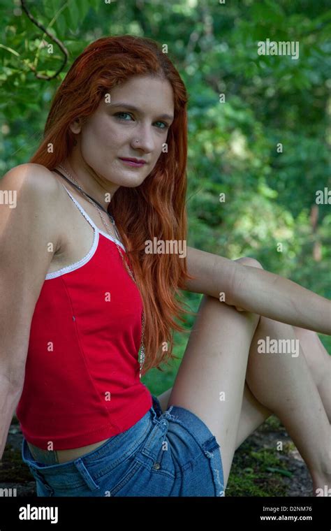 Lovely Redhead Woman Wearing A Red Top And Blue Jean Shorts Looking At The Camera With A