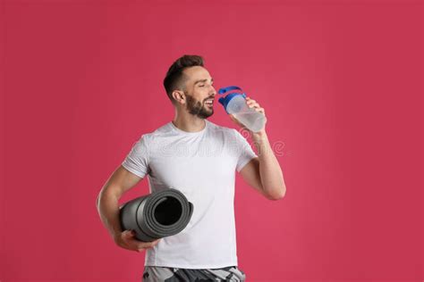 Handsome Man With Yoga Mat Drinking Water On Pink Background Stock