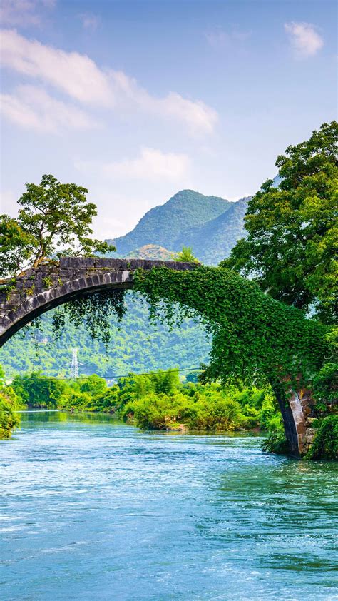 Arch Above River Between Green Trees With Landscape View Of Mountains