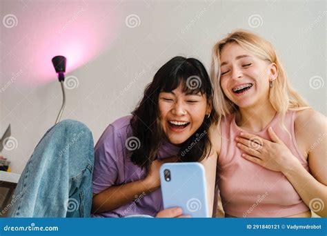 Two Multiracial Girls Using Mobile Phone While Eating Snacks Together Stock Image Image Of