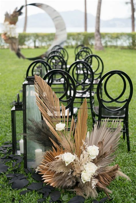 Aisle Flower Arrangement With Dried Palm Fronds Beside Black Chairs