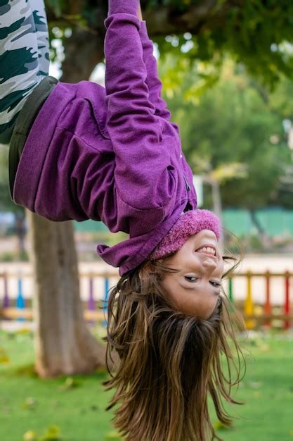 Premium Photo Portrait Of Smiling Girl Hanging Upside Down In Park