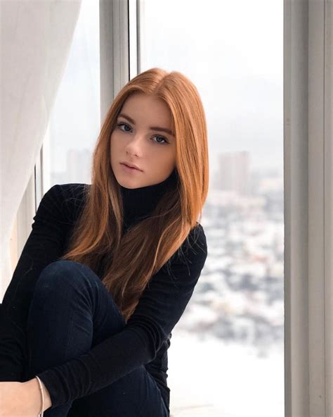 A Woman With Long Red Hair Sitting In Front Of A Window