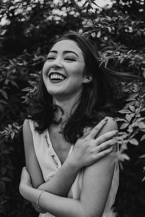 Black And White Photograph Of A Woman Laughing In Front Of Some Bushes With Her Hands On Her Chest