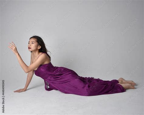full length portrait of pretty brunette asian girl wearing purple flowing gown sitting pose on