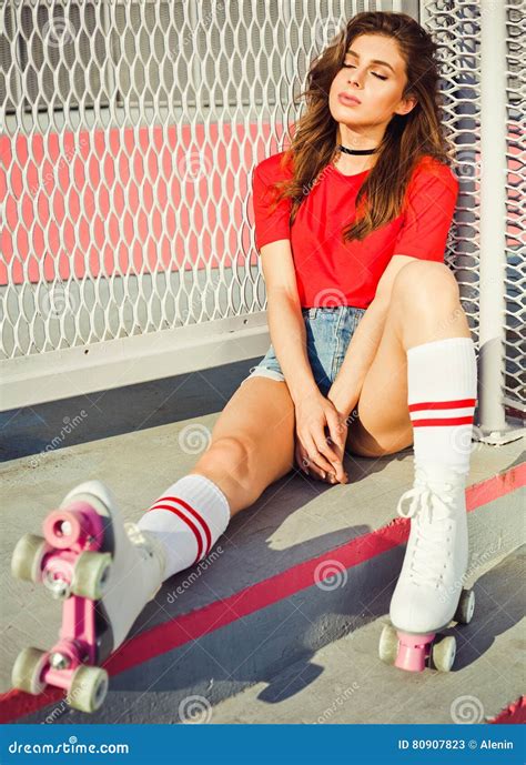 pretty brunette girl in a red top and jeans shorts and vintage roller derby has a rest sitting
