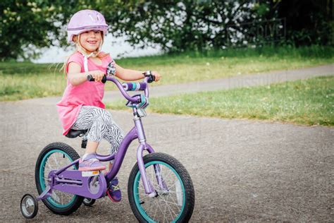 Mixed Race Girl Riding Bicycle With Training Wheels Stock Photo