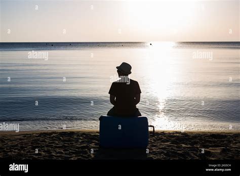 Man Silhouette Sitting Alone With Suitcase On Stony Beach And Watching Romantic Colorful Sunrise
