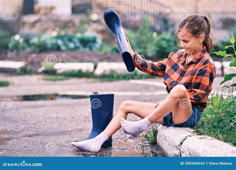 Teenage Girl Sitting On The Curb And Pouring Water From Rubber Boots Royalty Free Stock