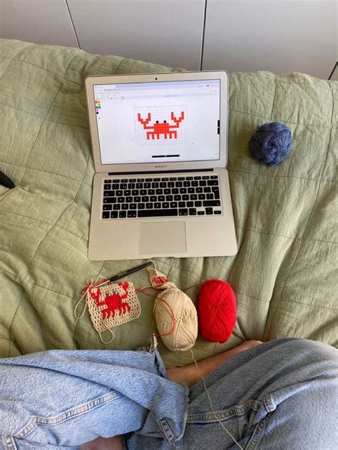 A Laptop Computer Sitting On Top Of A Bed Next To Balls Of Yarn And Crochet