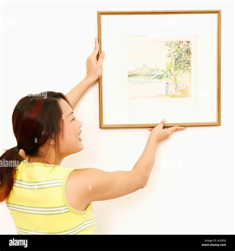 Rear View Of A Young Woman Mounting A Picture Frame On The Wall And