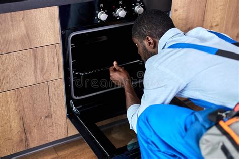 Young African Handyman Examining Electric Oven In Kitchen At Home