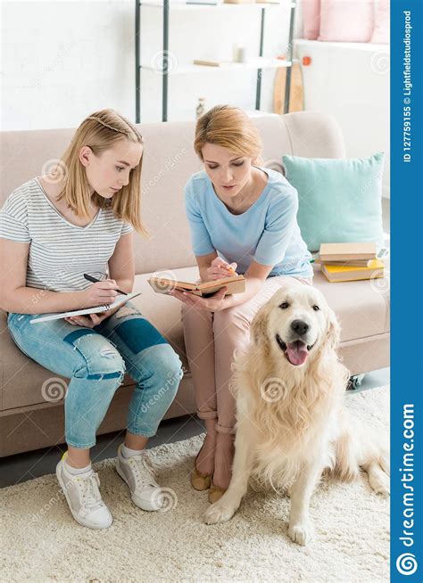 Mother And Teen Daughter Doing Homework Together While Their Dog