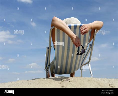 Woman Sunbathing On Deckchair On The Beach Shot Against Blue Sky Stock
