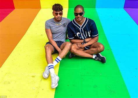 Two Men Sit On A Rainbow Flag Painted On The Pavement At Oxford Circus