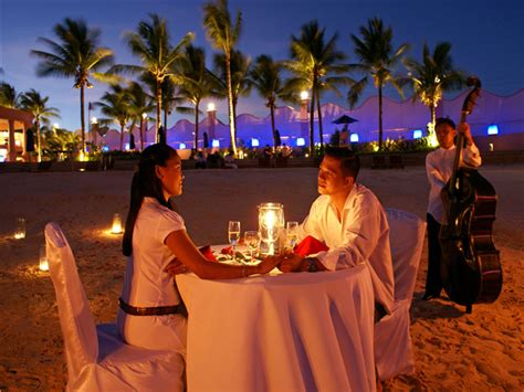 Two People Sitting At A Table With Candles In Front Of Them And Palm