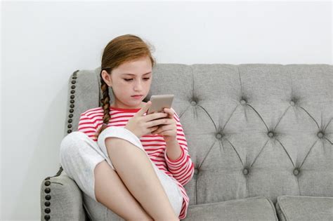 niña sentada en el sofá juega teléfono inteligente en la sala de estar foto premium