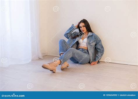 Beautiful Girl In Jeans Clothes Sitting On The Floor In A White Room