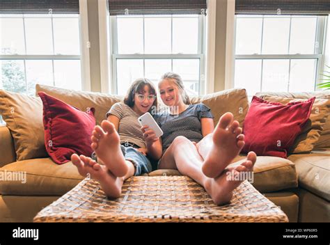 Two Teenage Girls Sitting On Couch With Feet Up Looking At Cellphone Stock Photo Alamy